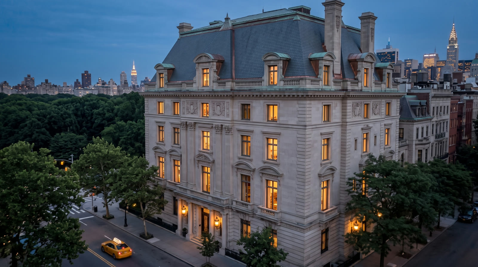 Drone view at rooftop height of the Beaux-Arts mansion's slate mansard and glowing windows